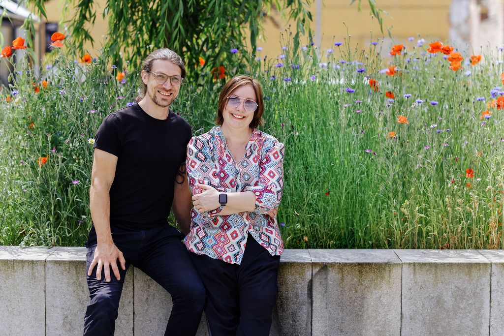 Falko Lange und Katrin Pappritz sitzen lächelnd vor einer Blumenwiese.
