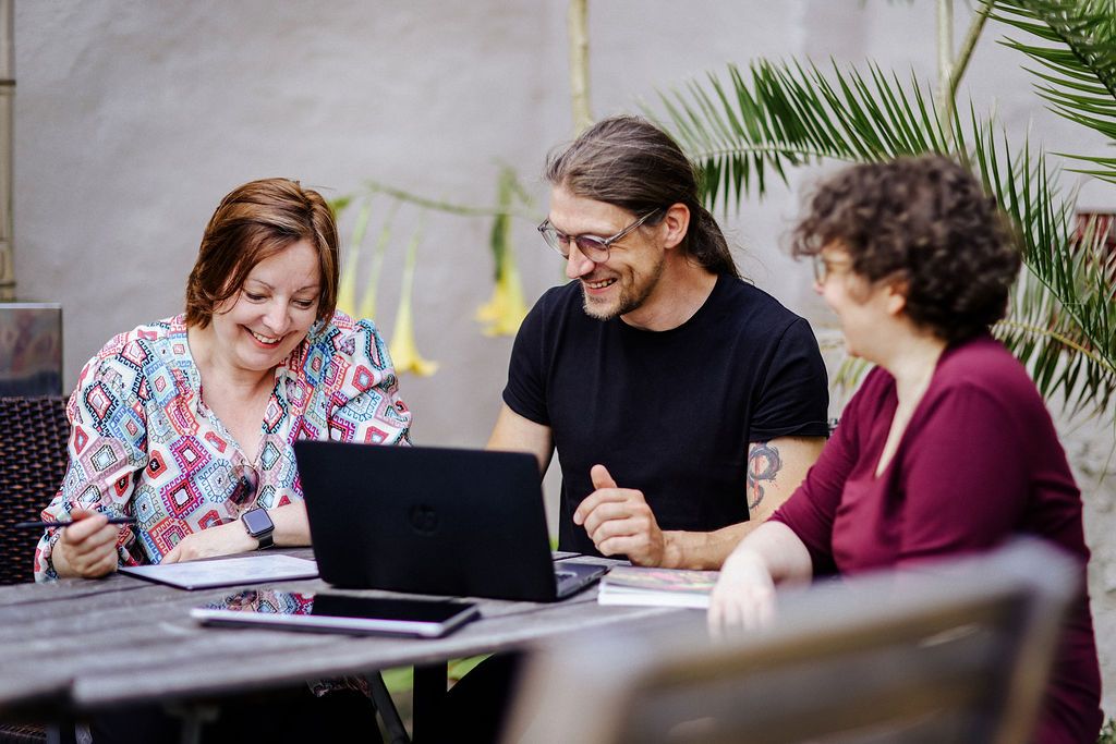 Katrin Pappritz, Falko Lange und eine Kollegin arbeiten lachend gemeinsam am Laptop.